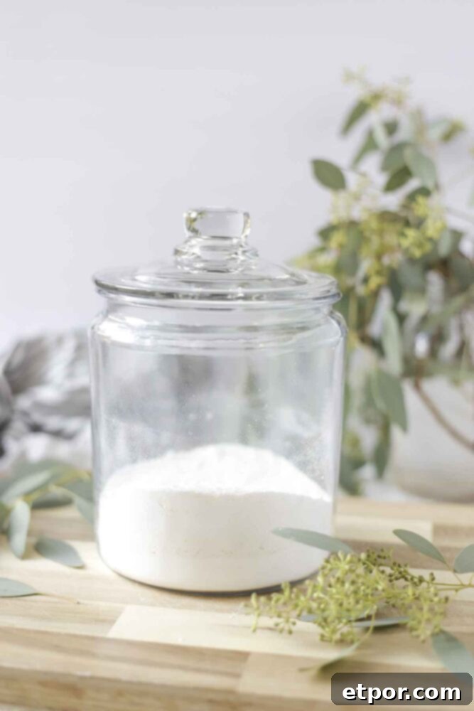 homemade laundry detergent in a glass dish with a lid on a wood cutting board with a mason jar full of eucalyptus