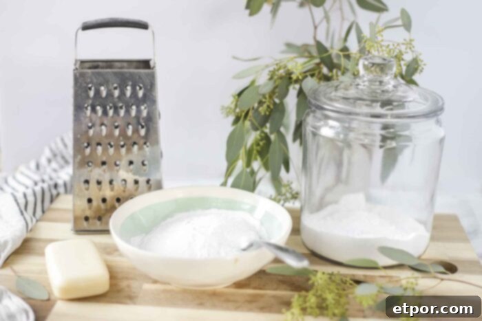 ingredients to make homemade laundry detergent on a wood cutting board with a cheese grater, and eucalyptus leaves behind