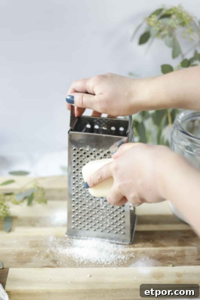 grating a bar of natural soap with a box cheese grater on a wood cutting board for homemade laundry detergent.