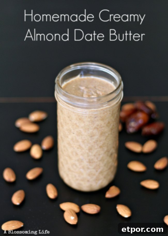 Homemade creamy almond butter in a glass jar, surrounded by whole almonds and pitted dates on a wooden surface.