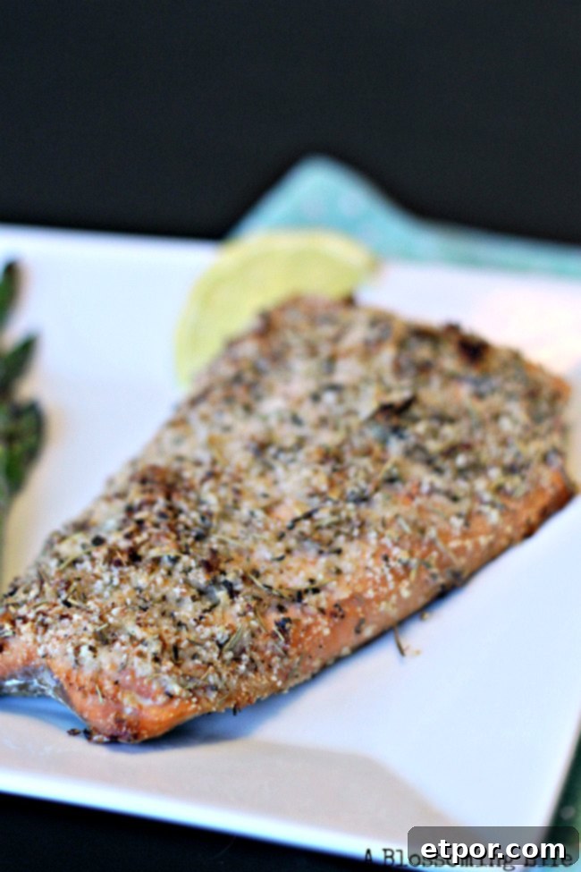 Italian crusted salmon on a white dish with lemon slice, garnished with fresh herbs