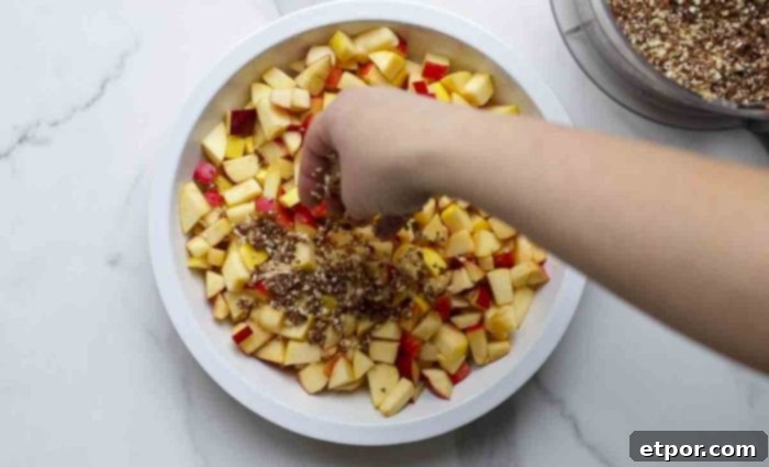 hand sprinkling crisp topping over apples in a pie plate