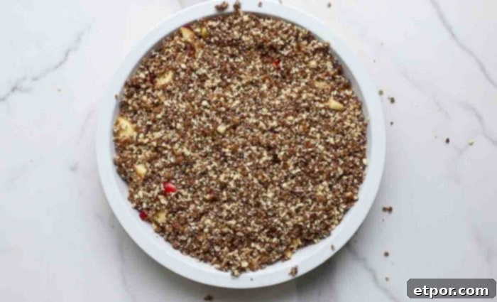 crumble topping on top of apples in a pie plate on a marble counter