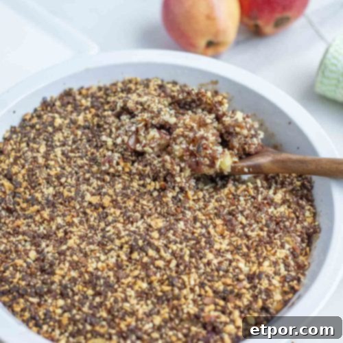 a pie plate full of healthy apple crisp topped with dates and almonds on a marble counter with apples in the background