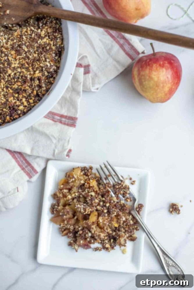 overhead photo of apple crisp on a small white plate on a marble countertop with a plat of apple crisp and apples in the background