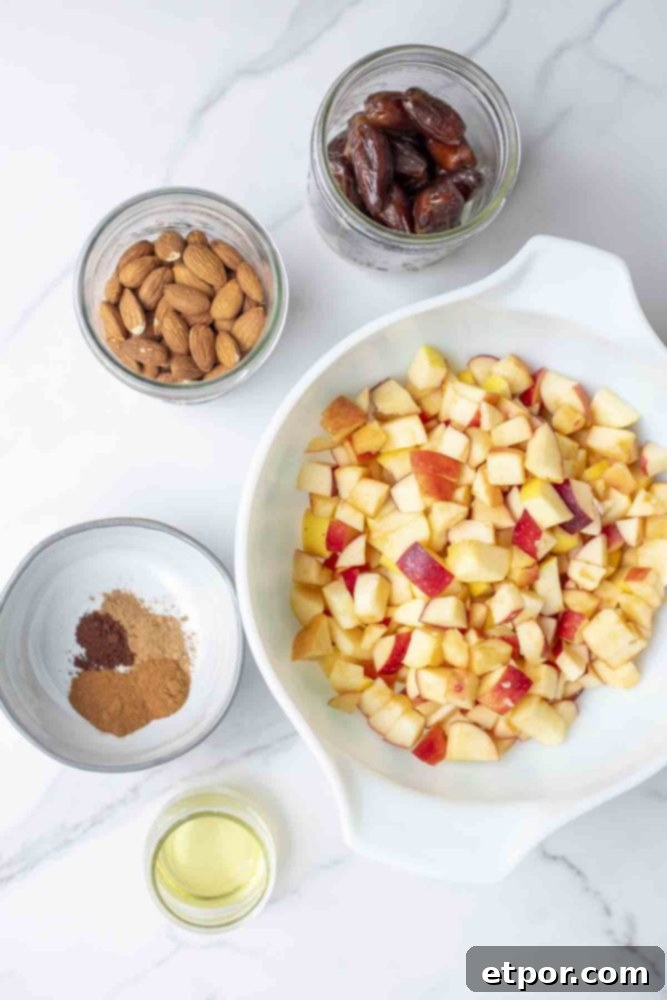 bowls and jars filled with apples, dates, almonds, spices and oil on a marble countertop