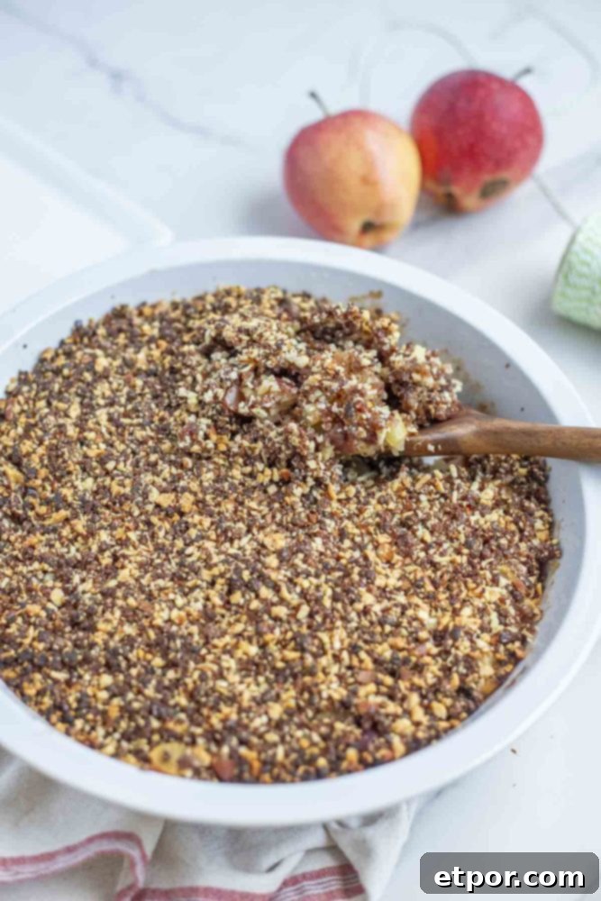 a pie plate full of healthy apple crisp topped with dates and almonds on a marble counter with apples in the background