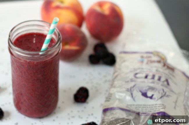 Berry peach Smoothie with Chia Seeds in a glass cup, surrounded by fresh blackberries, sliced peaches, and loose chia seeds on a white kitchen counter, highlighting healthy ingredients.