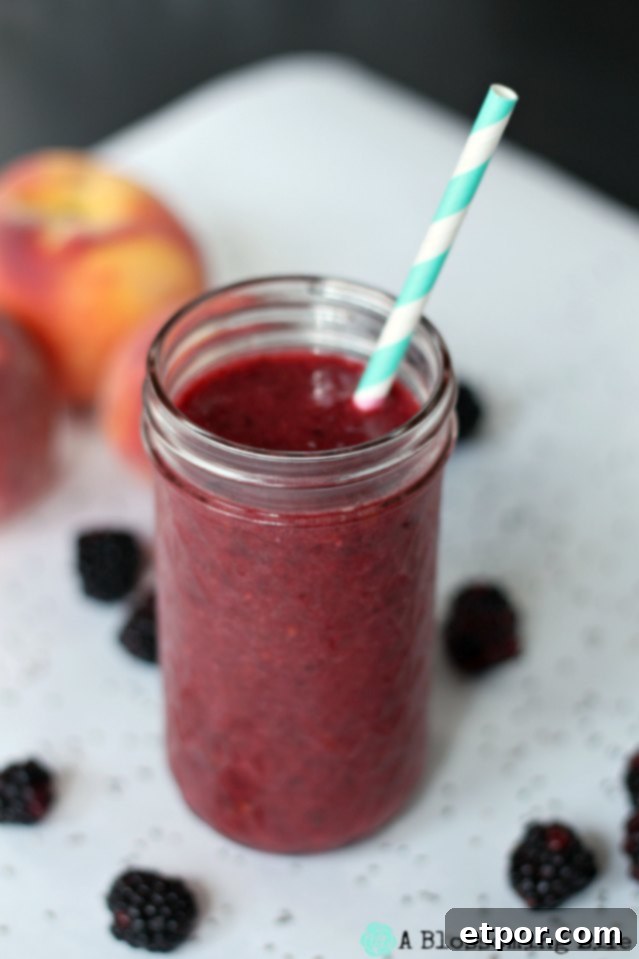Vibrant berry peach smoothie served in a glass jar with a stylish teal and white striped straw, set against a bright background, inviting a refreshing sip.
