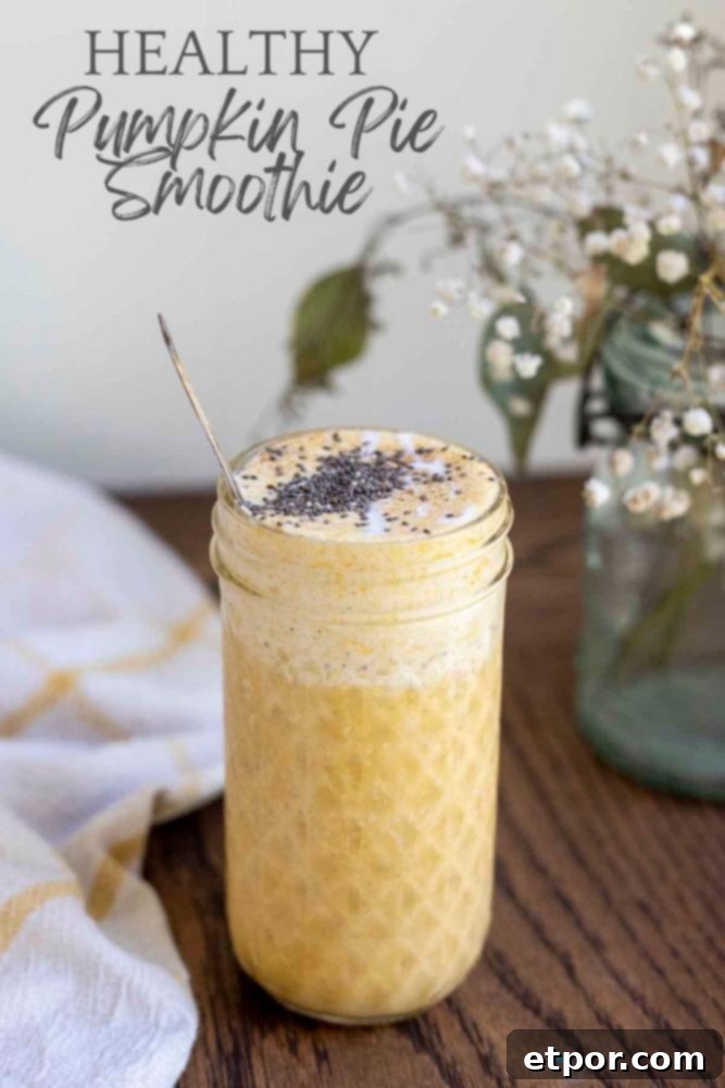 Spiced Pumpkin Pie Bliss Smoothie 2 healthy pumpkin spice smoothie in a glass jar on a wood countertop with a yellow and white towel and a jar of flowers in the background