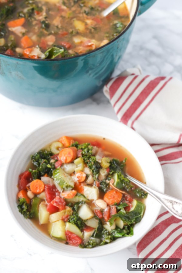 Smoky Bacon Minestrone Comfort Food 3 A rustic scene featuring a white bowl of classic minestrone soup next to an antique spoon and a red and tan napkin, with a large pot of minestrone simmering in the background.