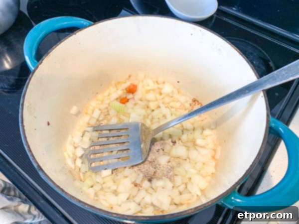 Diced onions cooking in bacon fat within a Dutch oven, becoming translucent for the minestrone soup.