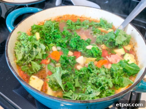 Fresh kale and sliced zucchini being added to a Dutch oven with minestrone soup, ensuring they cook just enough to soften.