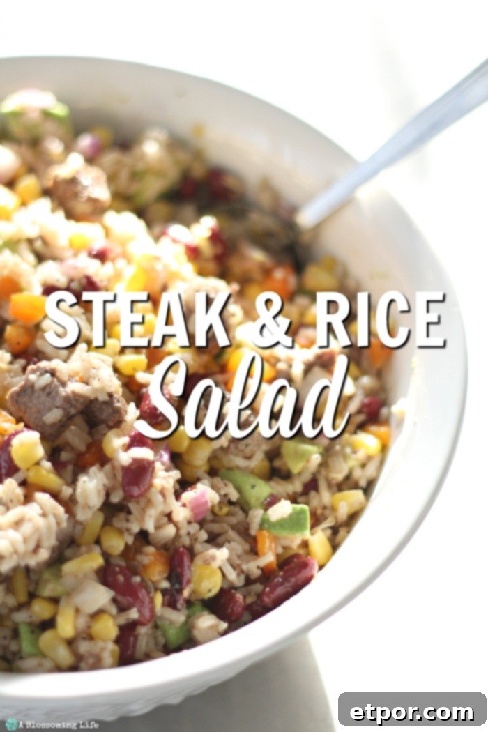 A vibrant Steak Rice Salad in a white bowl with a serving spoon, showcasing tender meat, fluffy rice, and crisp vegetables.