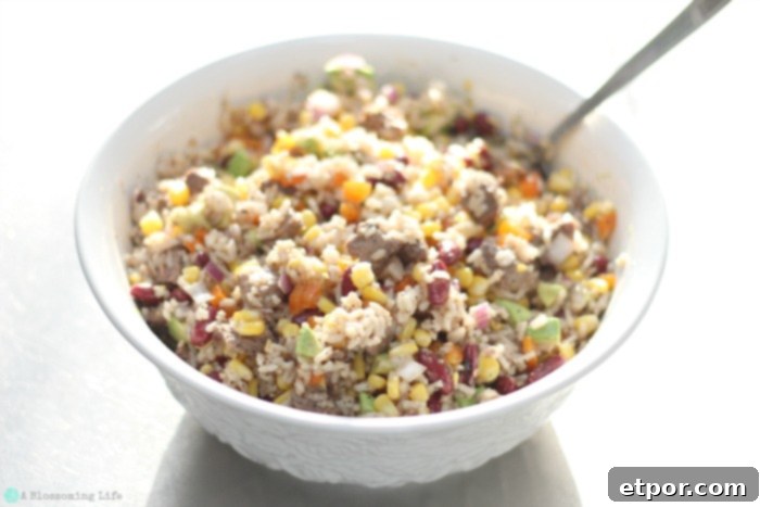 A large white bowl filled with Steak and Rice Salad, featuring visible pieces of cooked steak, corn, bell peppers, kidney beans, and avocado chunks, ready to be served.