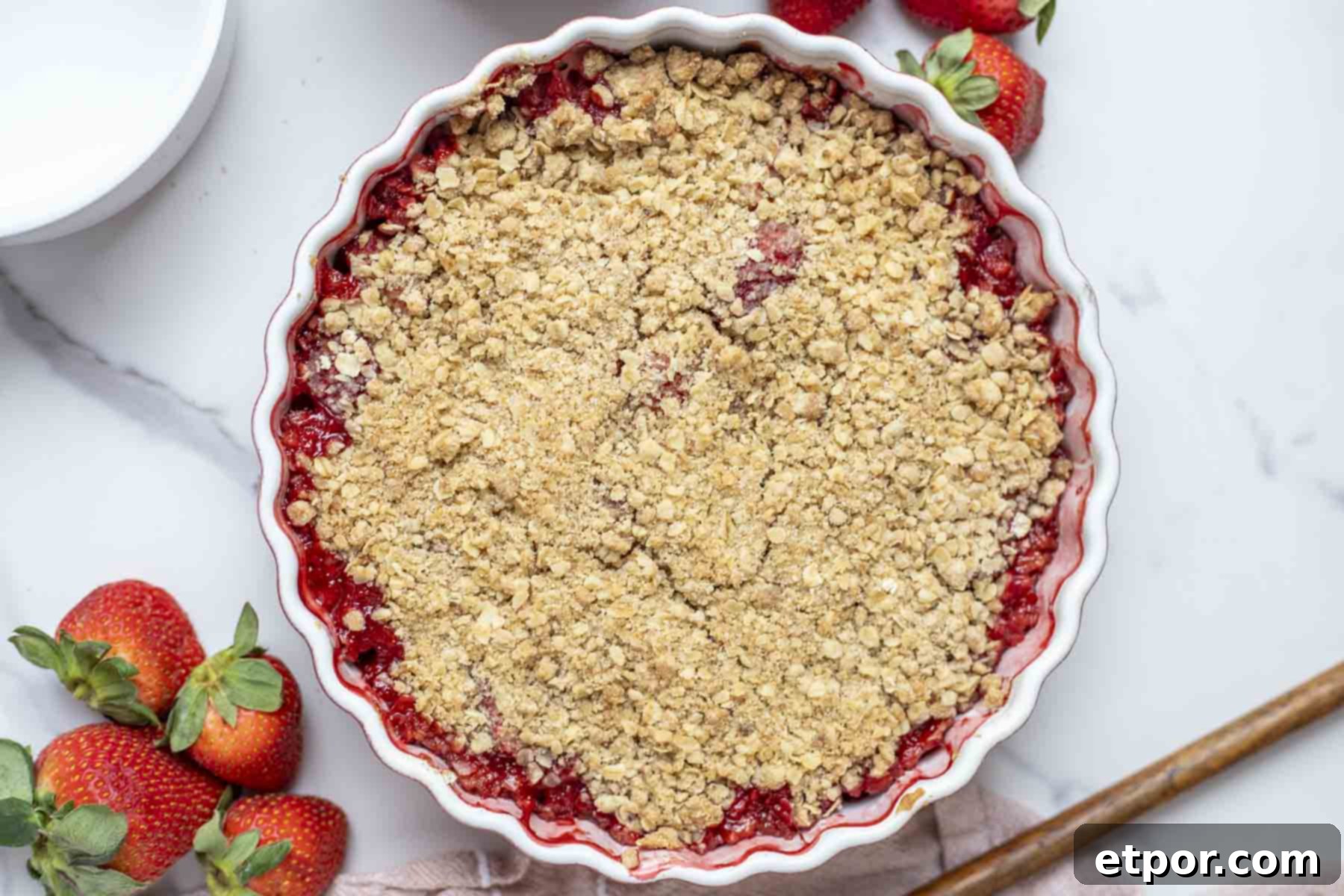 Simple Strawberry Crumble Bliss 4 Overhead photo of a strawberry crumble in a pie plate with strawberries surrounding the dish.