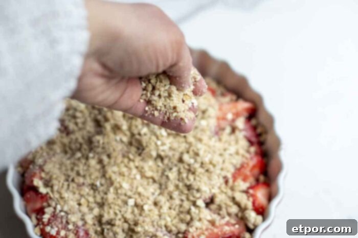 Simple Strawberry Crumble Bliss 8 sprinkling oat crumble over strawberries in a baking dish.