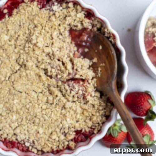 Strawberry crisp with a spoon in a baking dish surrounded strawberries.