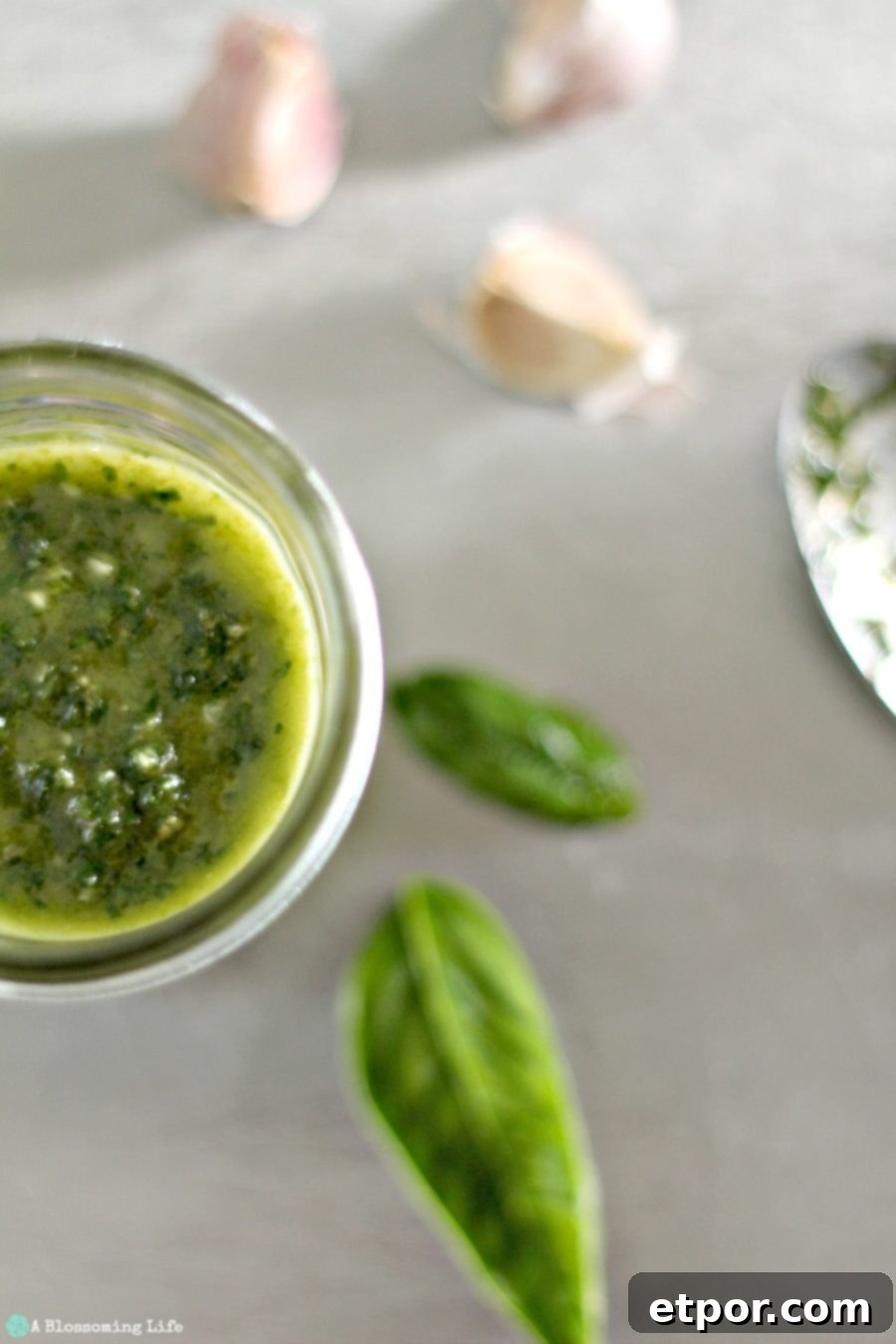 half of vegan pesto in a jar with basil and garlic cloves to the right