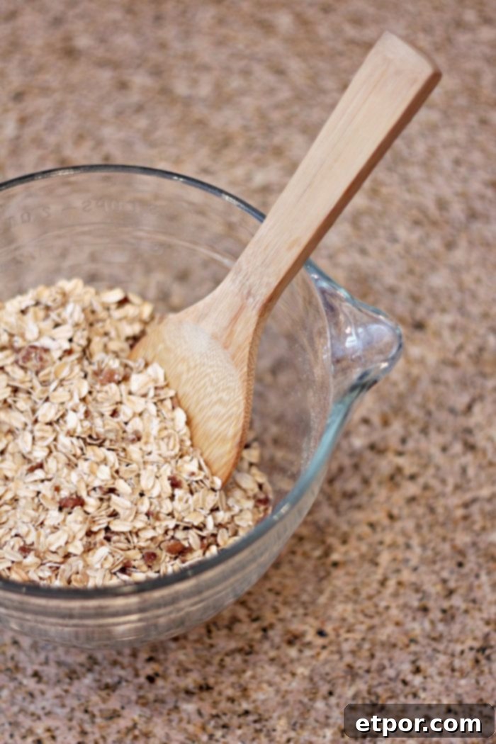 Whip Up Incredible Homemade Granola 2 A glass bowl filled with dry ingredients for homemade granola, including rolled oats, nuts, and seeds, ready for mixing. A wooden spoon rests in the bowl.