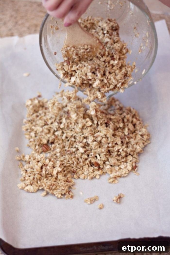 Whip Up Incredible Homemade Granola 3 Homemade granola mixture being poured onto a parchment-lined baking sheet, ready to be spread evenly and baked to perfection.
