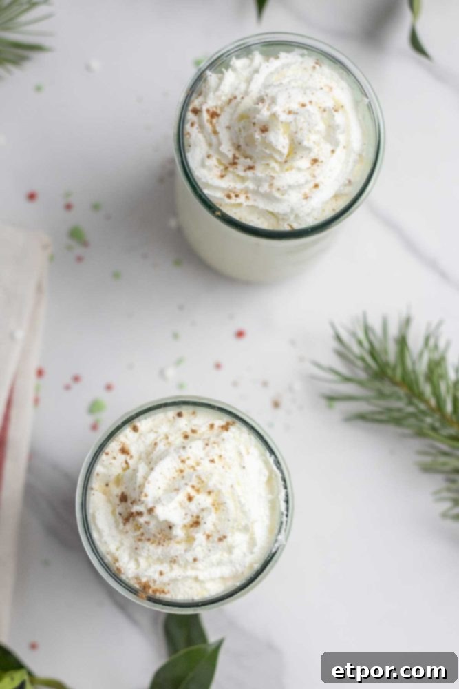 overhead photo of two glasses of eggnog on a white marble countertop surrounded by sprinkles and greenery