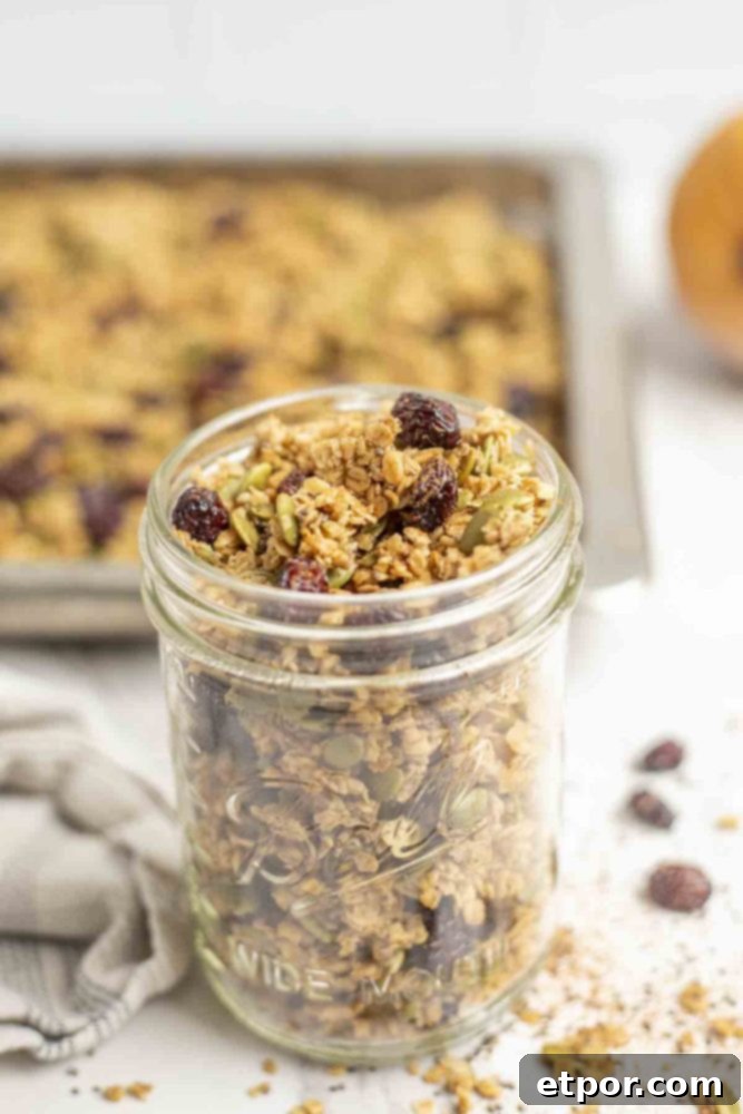 Irresistible Pumpkin Spice Granola 2 homemade pumpkin spice granola with dried cranberries in a mason jar on a marble countertop with a pan of granola in the background