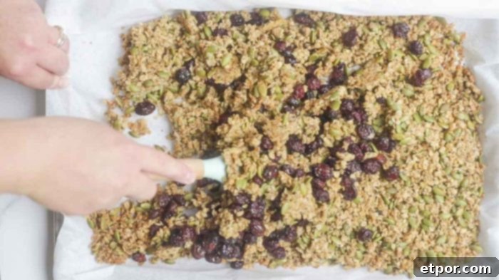 Irresistible Pumpkin Spice Granola 11 hand using a silicon spatula to mix together pumpkin spice granola with craisins