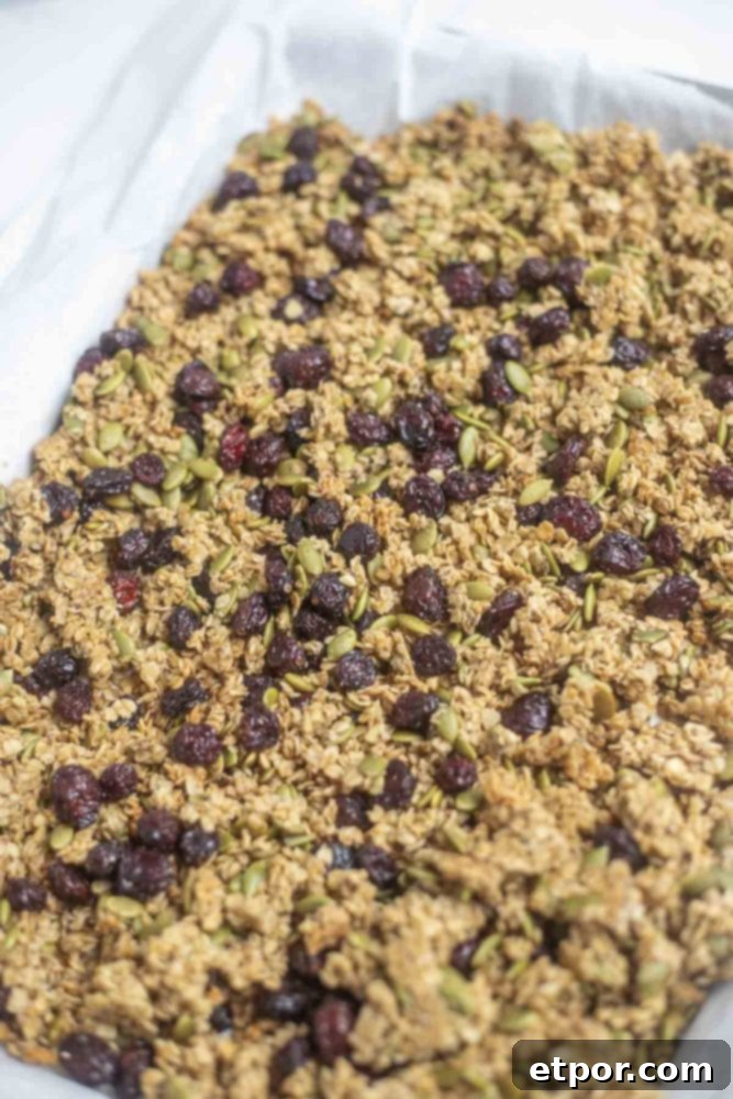 Irresistible Pumpkin Spice Granola 12 parchment lined sheet pan with pumpkin spice granola with pumpkin seeds and dried cranberries