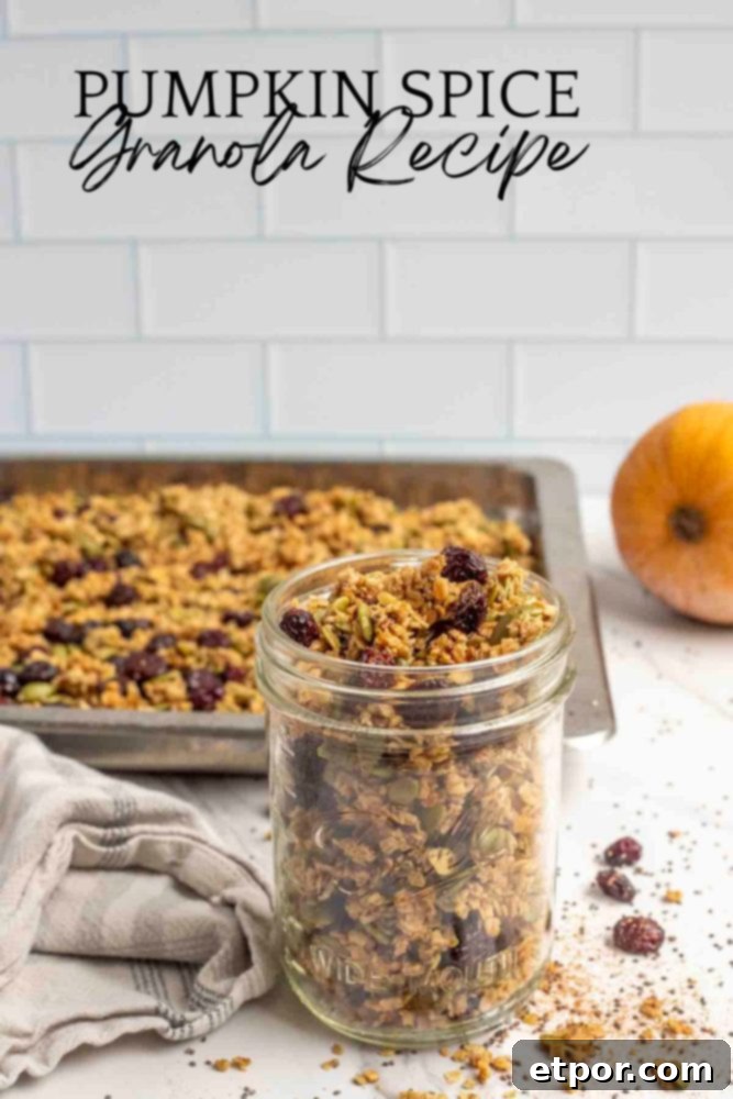 Irresistible Pumpkin Spice Granola 3 a jar of pumpkin granola with dried cranberries in a mason jar on a marble countertop with oats, chia seeds, and cranberries surrounding the jar. A pan of more granola and a pumpkin is in the background