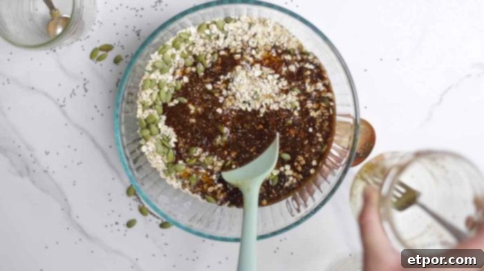 Irresistible Pumpkin Spice Granola 7 oats, pumpkin seeds, maple syrup, and other ingredients in a glass bowl on a marble countertop