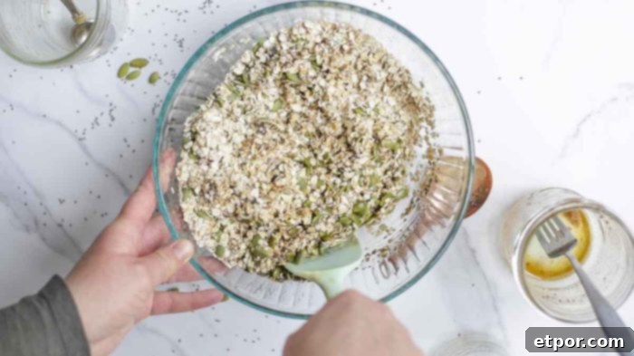 Irresistible Pumpkin Spice Granola 8 raw granola being mixed together in a glass bowl on a white marble countertop