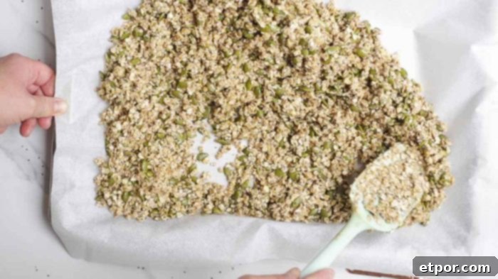 Irresistible Pumpkin Spice Granola 9 spreading a oat mixture onto a parchment lined baking dish