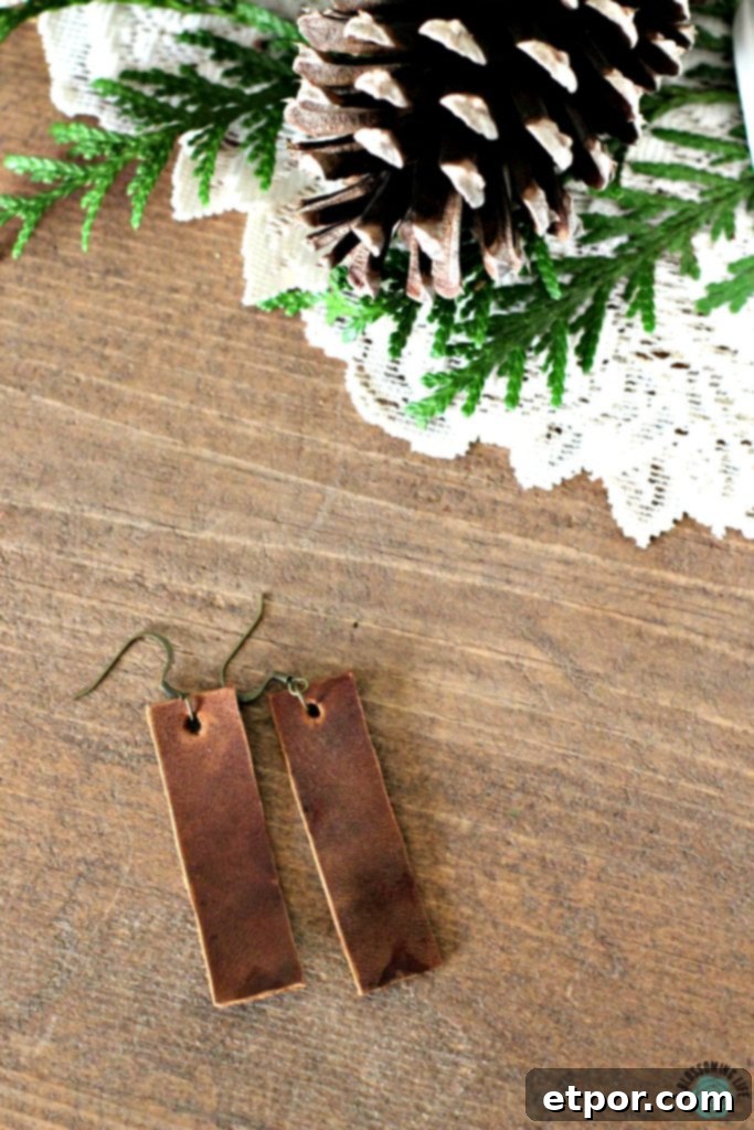 Pair of brown rectangular earrings laying on a table with pine cones on a while fabric doily behind it