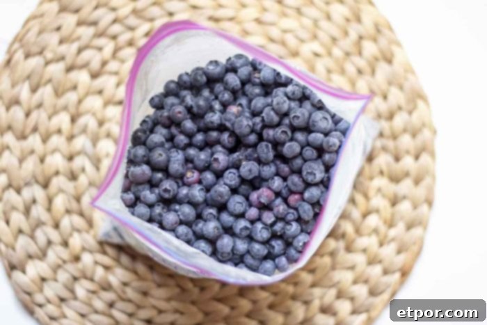 Overhead shot of a partially filled freezer bag of frozen blueberries on a woven mat, ready for easy storage.