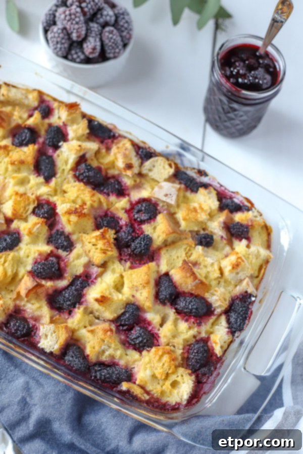 Baked French toast casserole generously topped with fresh blackberries and a jar of homemade maple blackberry syrup