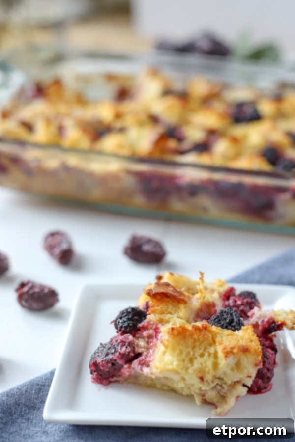 A perfectly baked slice of French Toast Casserole with vibrant blackberries, with the full baking dish in the background