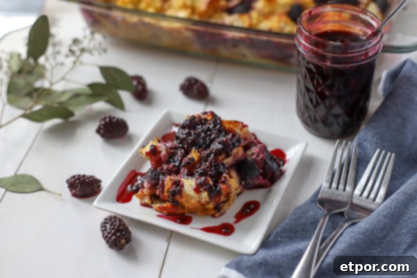 A close-up of a slice of French Toast Casserole generously covered with luscious blackberry syrup, with the baking dish visible behind it