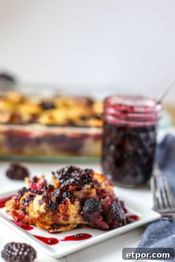 A beautiful slice of baked French toast casserole with a generous drizzle of blackberry syrup, accompanied by the full casserole dish and a jar of syrup