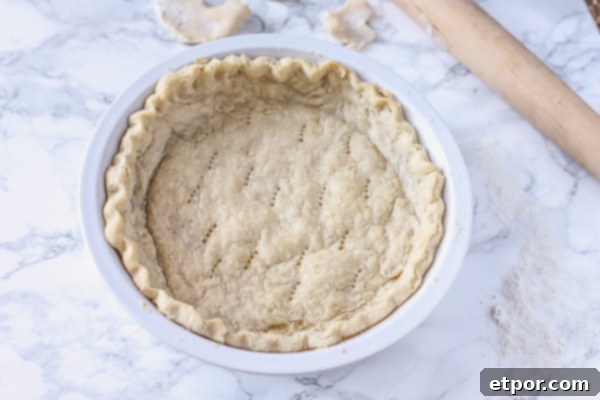Baked gluten free pie crust in a white pie pan setting on a marble counter with extra dough and a rolling pin.