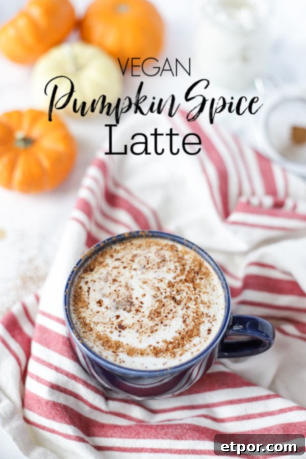 vegan pumpkin spice latte with pumpkin spice sprinkled on top in a blue mug on top a tan and red towel with mini pumpkins behind