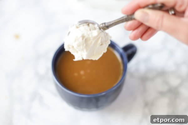 adding a large spoonful of vegan whipped cream into a vegan pumpkin spice latte