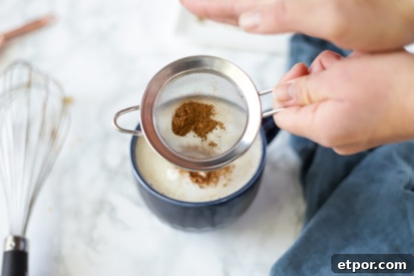 topping a vegan pumpkin spice latte with pumpkin spice using a sifter