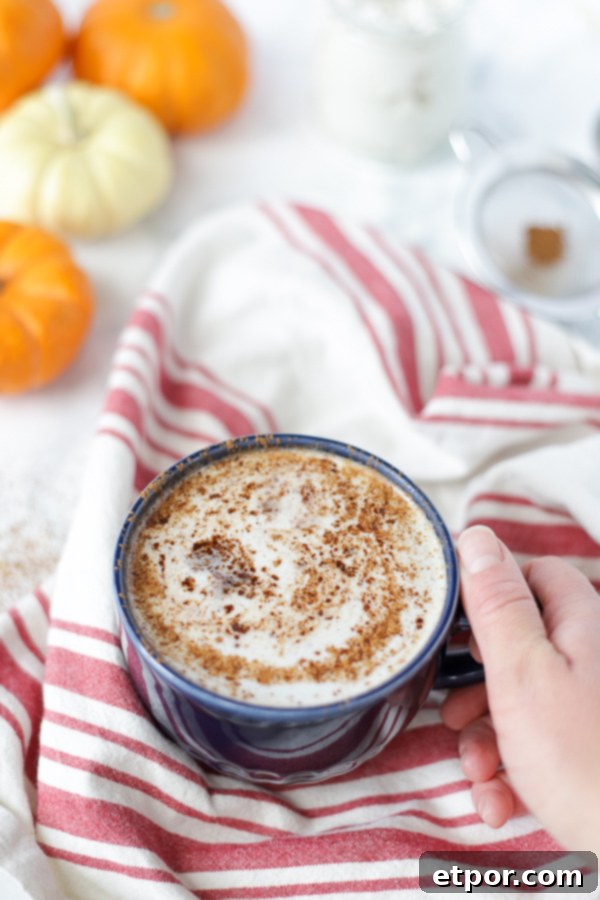 hand holding a blue mug with a frothy vegan pumpkin spice latte