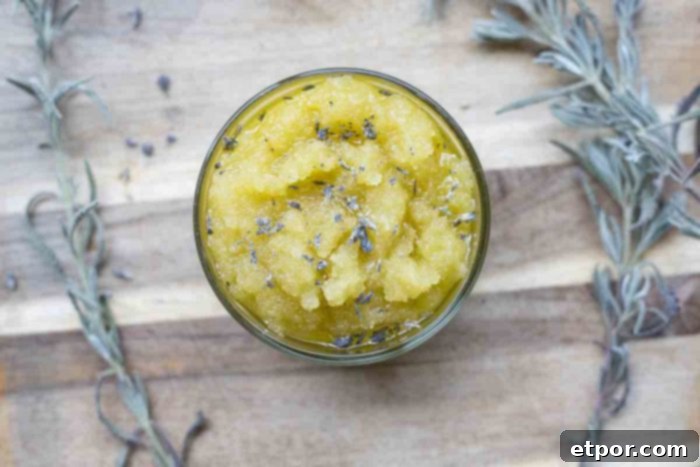 Homemade Lavender Bliss Body Polish 2 overhead photo of a jar of lavender scrub topped with dried lavender on a wood cutting board. Lavender sprigs surround the jar