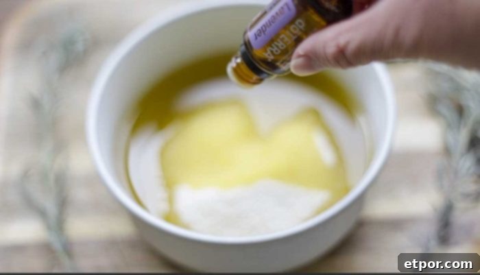 Homemade Lavender Bliss Body Polish 6 essential oil being dripped into a bowl of oil and sugar on a wood cutting board