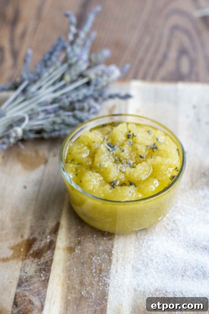 Homemade Lavender Bliss Body Polish 10 sugar scrub with lavender essential oil on a wood cutting board with a bundle of lavender behind the jar