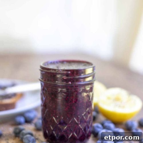 jar of homemade blueberry chia jam on a wood table with blueberries spread around and sliced lemons