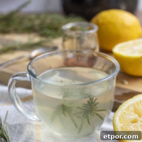 rosemary tea with fresh sprigs of rosemary in a glass mug with sliced lemons surrounding the muffin