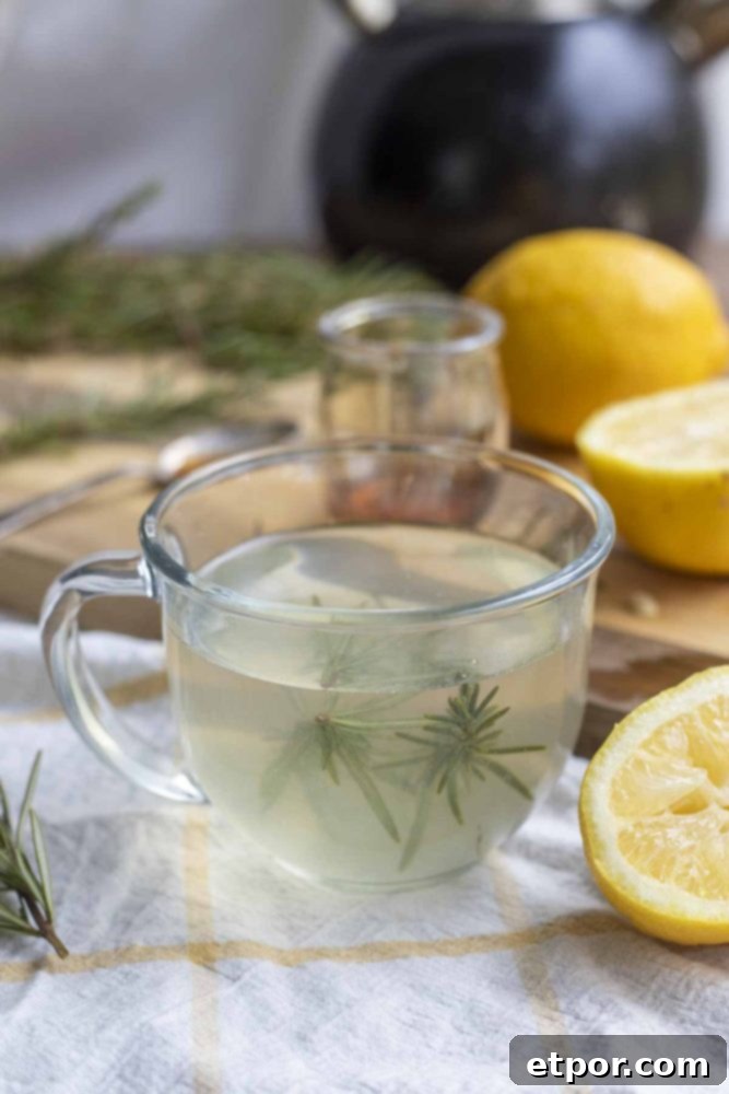rosemary tea with fresh sprigs of rosemary in a glass mug with sliced lemons surrounding the muffin